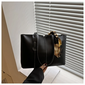 Close-up of black leather tote bag with white contrast stitching and printed silk scarf