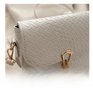 Close-up of white crossbody bag featuring embossed crocodile pattern and gold buckle