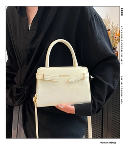 Gros plan du sac bandoulière crème avec boucle dorée et lettrage porté par un mannequin