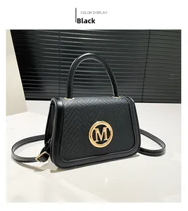 Detail of black leather handbag with woven texture flap and golden M logo hardware