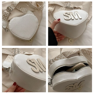 Detail of white heart-shaped bag with metal SM logo and woven geometric shoulder strap