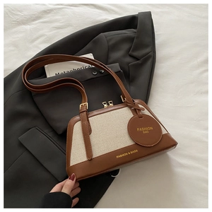 Detail of color-block tote bag with leather texture and brand tag on grey blazer