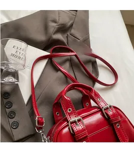 Detail of red glossy leather handbag with adjustable silver buckle strap and zippers
