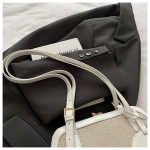 Detail of cream woven fabric texture and white leather handles on a shell crossbody bag