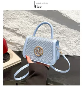 Detail of light blue box bag featuring woven flap and circular golden M metal logo