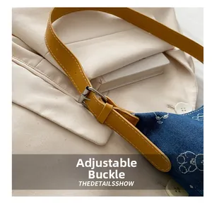 Detail of silver metal buckle on yellow leather strap of blue denim cat print bag