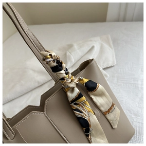 Detail of taupe tote bag featuring geometric stitching and a patterned silk scarf handle