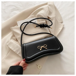 Close-up of golden bow hardware on premium black leather crossbody handbag texture