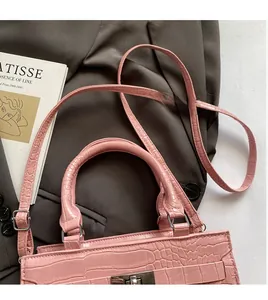Pink crocodile-embossed handbag featuring metal turn-lock and detachable shoulder strap