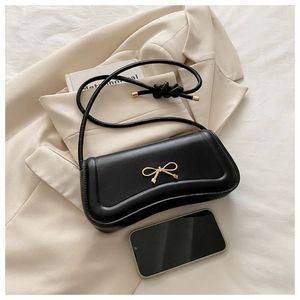 Detail view of black faux leather handbag with golden metal bow and elegant rope knot handle