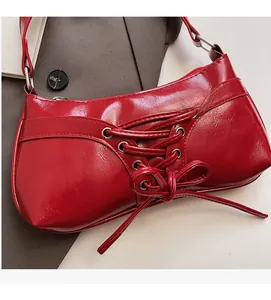 Detail of red patent leather shoulder bag with decorative lace-up bow and silver hardware