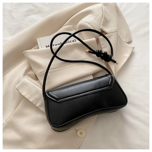 Detail of black leather handbag with knotted strap accent on elegant beige blazer backdrop