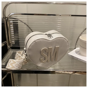 Detail of heart-shaped cream bag with metal SM logo and patterned wide woven strap