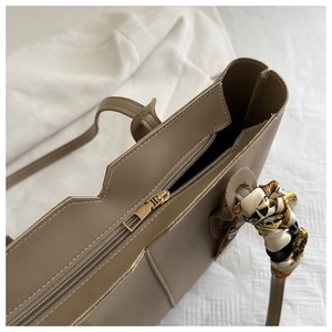 Close-up of taupe tote bag with gold zipper closure and patterned silk scarf detail