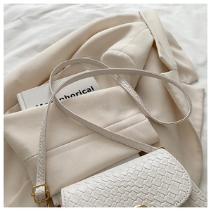 Close-up of white woven texture shoulder bag with gold metal clasp on beige suit