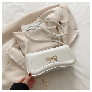 Detail of white PU leather crossbody bag featuring a golden metal bow and knotted strap