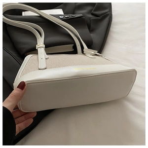 Close-up of a minimalist cream leather and canvas shell bag showing the bottom and side texture