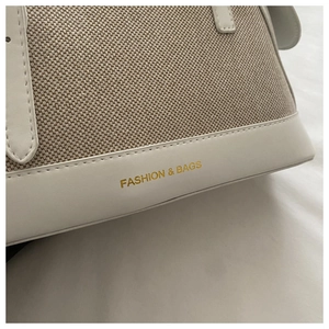 Close-up of canvas shell bag showing leather trim and gold FASHION & BAGS lettering