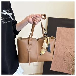 Detail of brown leather tote bag with V-cut design and decorative handle silk scarf
