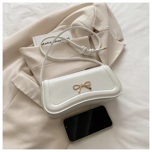 Detail of white leather baguette bag with golden bow hardware and phone for scale
