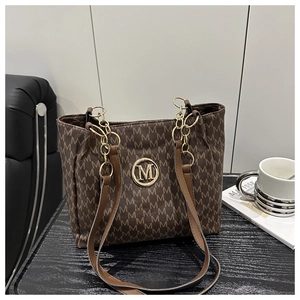 Detail of brown tote bag with classic M-monogram pattern and golden metal logo charm