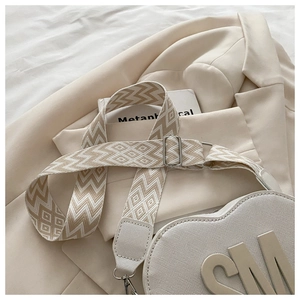 Detail of cream heart-shaped crossbody bag with embossed SM logo and woven jacquard strap