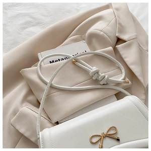 Detail of elegant white crossbody bag featuring a golden bow buckle and knotted strap