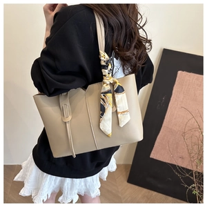 Detail of beige tote bag with V-cut design and printed silk scarf on handle for women