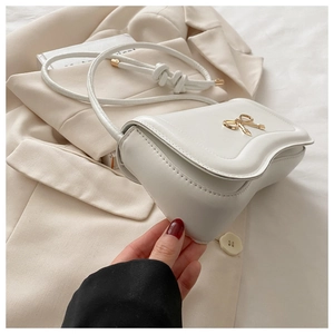 Detail of white wave-edge crossbody bag with gold bow lock on a beige blazer