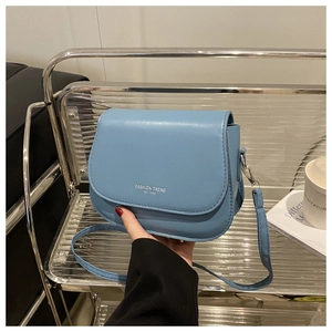 Detail view of light blue saddle bag featuring silver fashion trend logo and PU leather texture