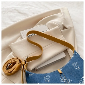 Close-up of blue denim underarm bag with white bear print and yellow leather strap