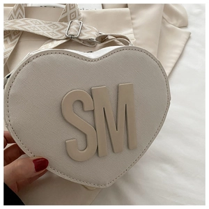 Detail of cream heart-shaped PU bag featuring embossed SM letters and patterned strap