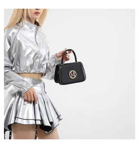 Detail of black textured handbag featuring a signature gold M metal logo and top handle