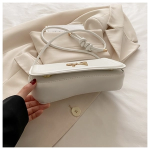 Detail of white leather crossbody bag featuring a golden bow buckle and knotted strap