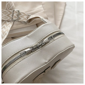 Close-up of beige Saffiano leather bag with silver zippers and geometric jacquard strap