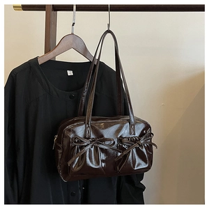 Detail of dark brown glossy patent leather underarm bag with decorative bow pockets