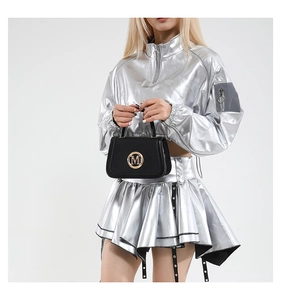Detail of a chic black handbag featuring a metallic round M logo on a stylish silver outfit