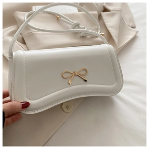 Close-up of white crossbody bag with gold bow clasp on elegant beige blazer