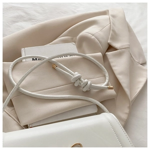 Close-up of white leather handbag with knotted strap and gold hardware accents