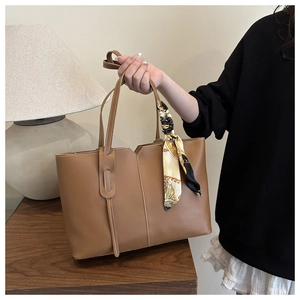 Detail of camel tote bag with V-shaped notch and decorative silk scarf on handle
