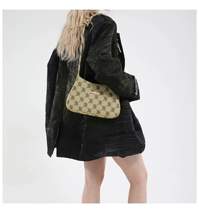 Dettaglio borsa baguette beige con monogramma e fibbia dorata su modella con cappotto nero