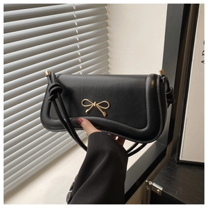 Detailed close-up of a black leather handbag with a gold metal bow and knotted strap handle