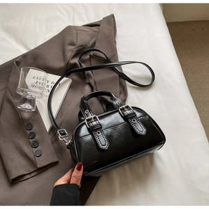 Close-up of black oil-wax leather handbag with twin handles and metallic buckle details