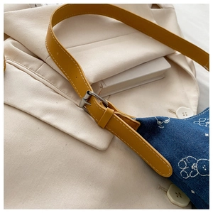 Detail of blue denim shoulder bag featuring cartoon bear print and yellow leather strap