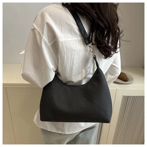Détail du sac hobo en cuir noir texturé avec boucles dorées porté à l'épaule