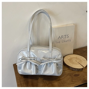 Dettaglio della borsa a spalla grigio chiaro lucida con tasche con fiocco sul tavolo