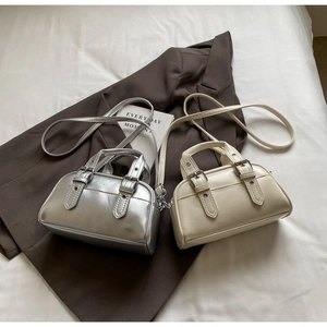 Detail view of silver and cream Boston bags with buckle straps on a brown blazer