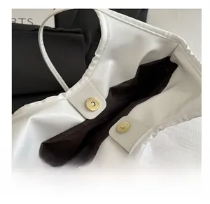 Detailed view of the magnetic gold-tone snap closures on a white lace tote bag