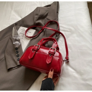 Detailed shot of vibrant red wax-leather Boston bag with metallic eyelets on a suit