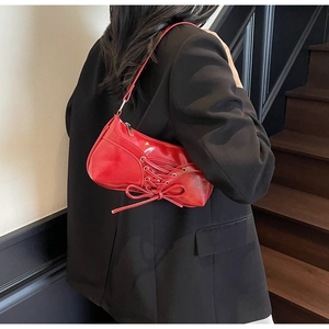 Detail of red patent leather shoulder bag featuring ribbon bows and metallic zipper